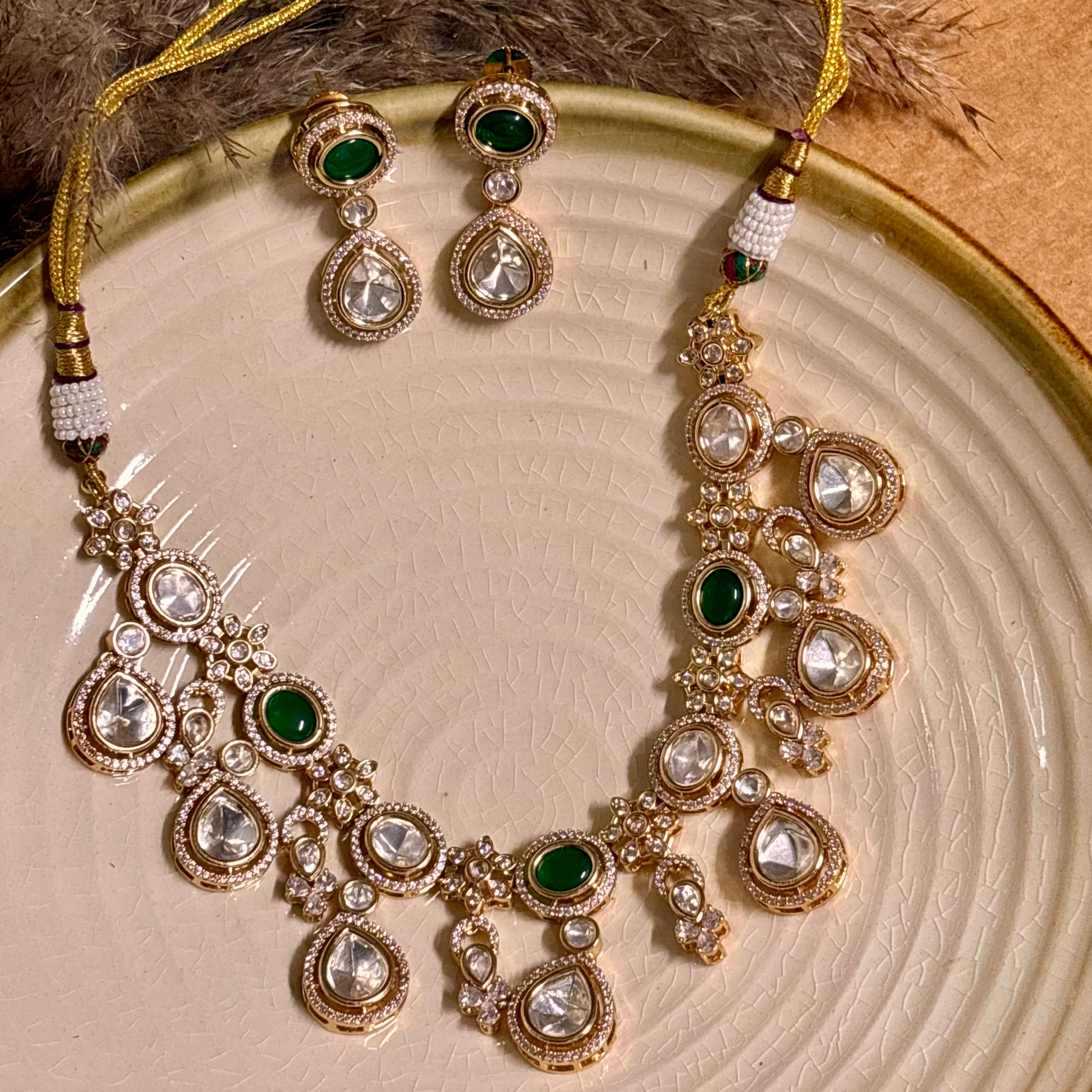 A gold-plated choker necklace with green stones and kundan detailing, paired with matching earrings, displayed on a plate.