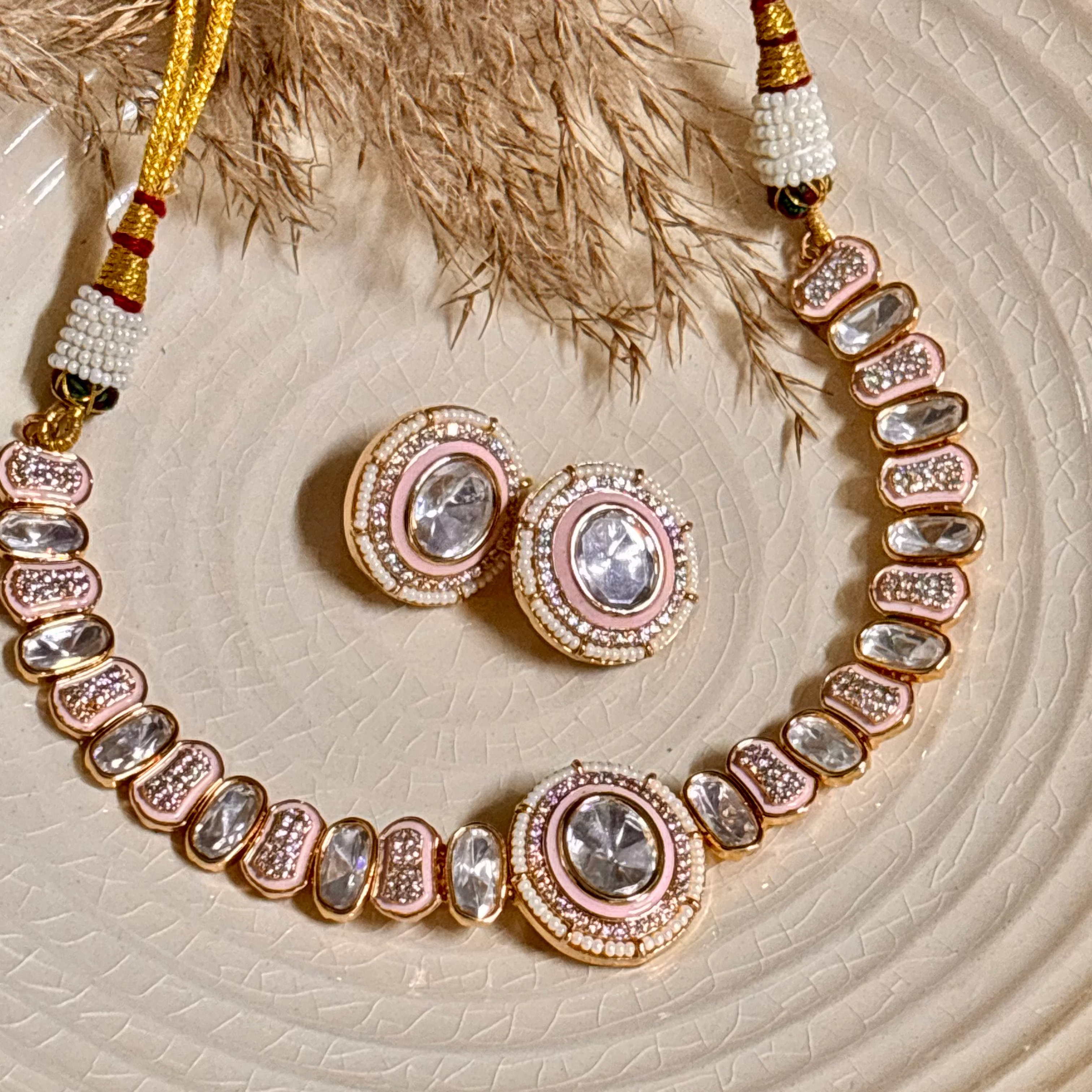 A pink Polki choker necklace set with matching earrings, handcrafted with gold-plated brass, pearls, carved beads, and semi-precious stones, displayed on a plate.