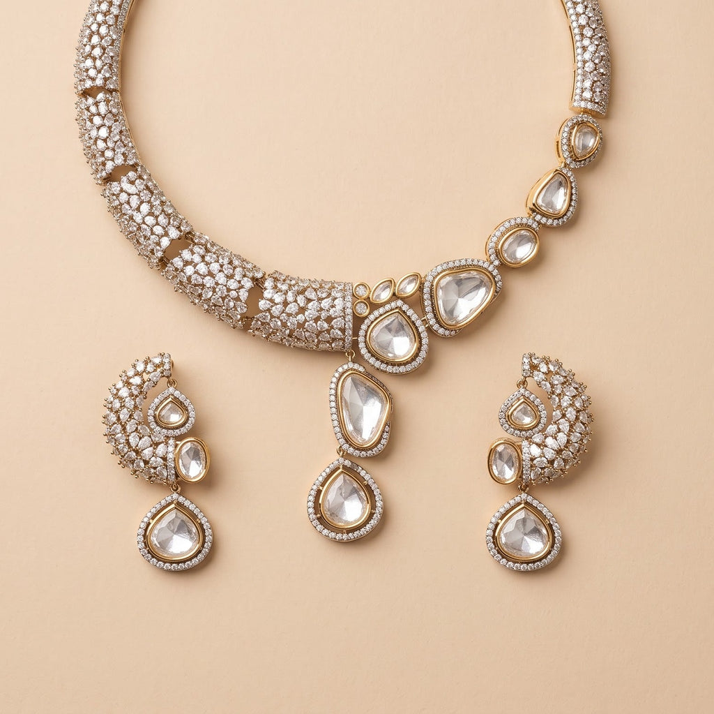 Gold-toned traditional Indian jewelry set featuring a necklace, earrings, and a pendant, embellished with clear stones on a warm beige background.