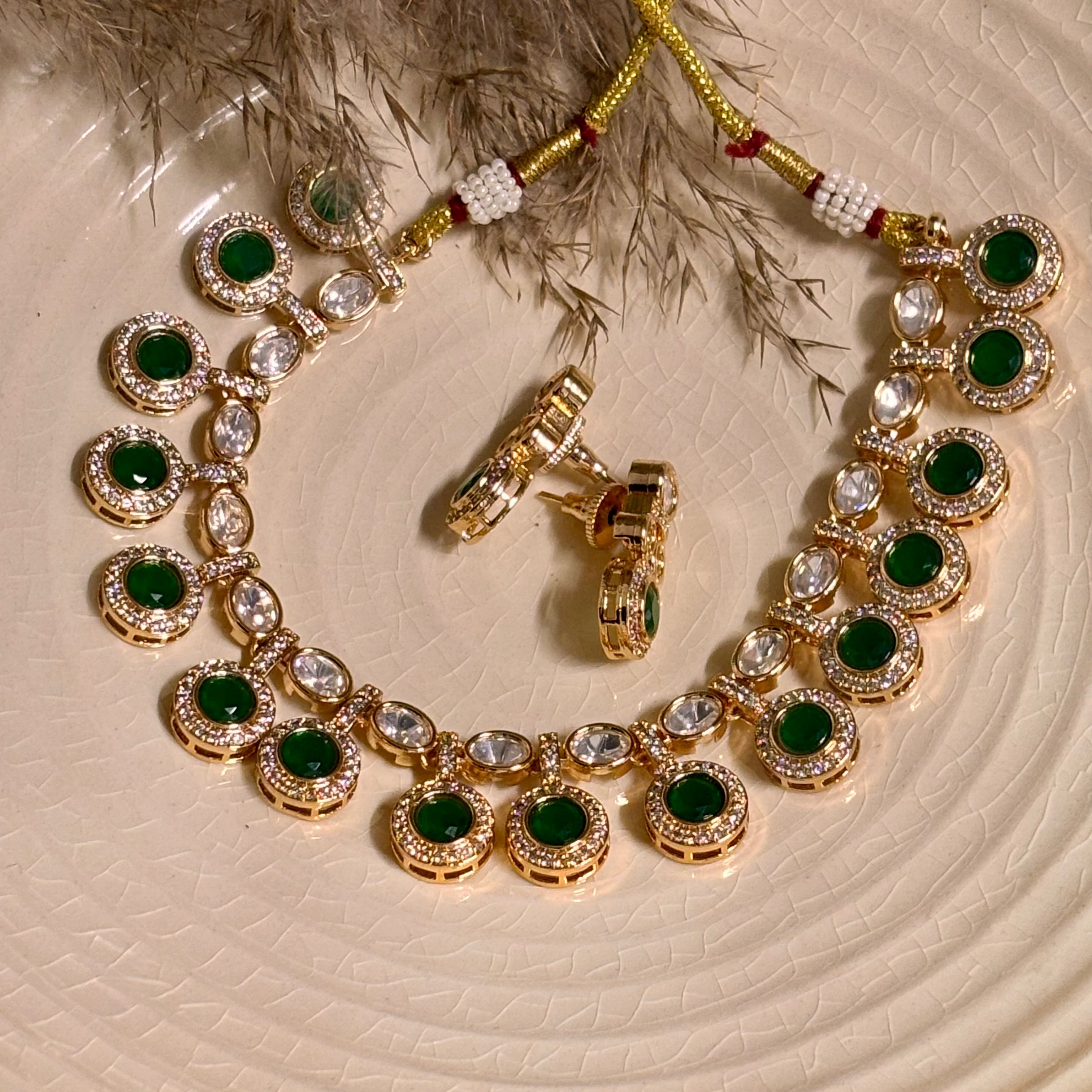 A gold-plated choker necklace with green stone accents and intricate Polki and Kundan work, displayed on a white plate.
